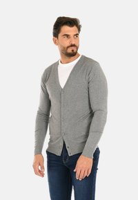 Cardigan grigio lavorato a maglia con scollatura a V, dotato di cinque bottoni e polsini a coste. Abbinato a jeans in denim blu.