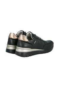 Zapatillas de cuero negro con una textura suave, que presentan acentos metálicos dorados en el talón y una gruesa suela de goma negra con textura.