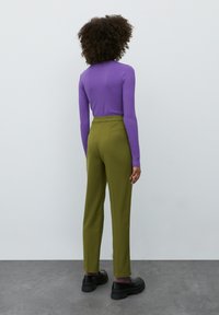 Geribbelde paarse langemouwen top gecombineerd met hoogwaardige olijfgroene broeken, aangevuld met zwarte chunky schoenen en een gladde textuur achtergrond.
