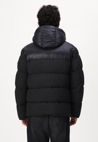 Giacca a vento nera con cappuccio lucido e superficie superiore liscia, caratterizzata da un motivo trapuntato e una vestibilità comoda, adatta per il freddo.