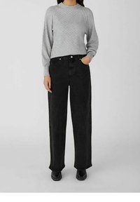 Grijze textuurtrui met lange mouwen, gecombineerd met hooggeknoopte zwarte denim jeans, beide met een ontspannen pasvorm en minimale details.