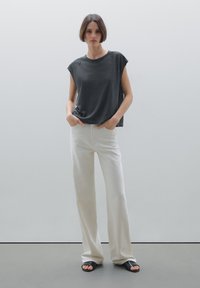 T-shirt grigio a maniche corte abbinato a pantaloni bianchi larghi e sandali neri a ciabatta. Tessuto morbido con un design casual.