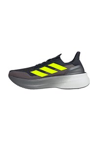 Chaussure de sport noire avec un logo à trois rayures jaunes vives, une tige texturée et une épaisse semelle intermédiaire blanche avec une semelle extérieure grise.