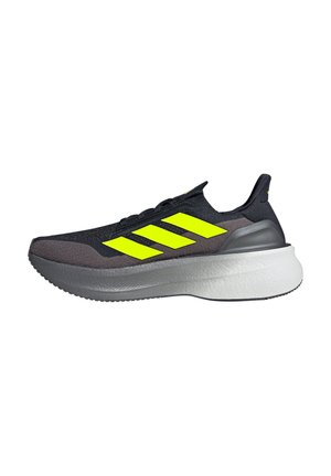Chaussure de sport noire avec un logo à trois rayures jaunes vives, une tige texturée et une épaisse semelle intermédiaire blanche avec une semelle extérieure grise.