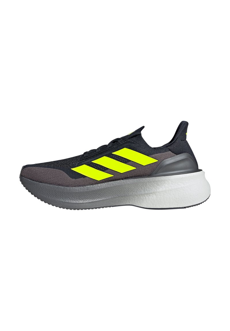 Chaussure de sport noire avec un logo à trois rayures jaunes vives, une tige texturée et une épaisse semelle intermédiaire blanche avec une semelle extérieure grise.