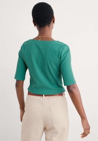 Zeleni rebrasti pleteni top s opuštenim krojem, s kratkim rukavima i širokim izrezom. Uparen s svijetlosmeškim hlačama visokog struka.