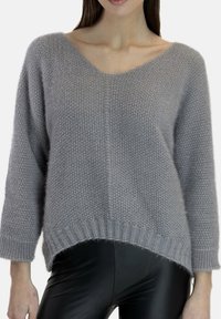 Lysegrå oversized strikket trøje med V-hals, lange ærmer og ribstrikket kant. Båret med sorte læderleggings.