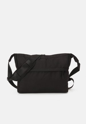 Sac bandoulière rectangulaire noir avec bandoulière réglable, poche avant zippée et fermeture double zip en haut sur fond uni.