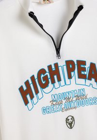 Sudadera de cremallera blanca con textura acanalada. Presenta "HIGH PEAK" en texto marrón y azul, junto con gráficos y logotipo adicionales con temática al aire libre.