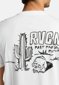 Hvid bomulds t-shirt med et sort linjekunstdesign af en kaktus og et kranium, med teksten "RVCA PAST PRESENT FUTURE."