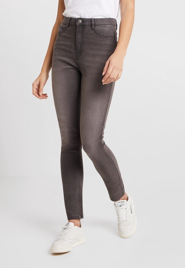 Jeans skinny grises con una textura suave, de cintura alta, bolsillos delanteros y un ligero desvanecimiento, combinados con zapatillas blancas.