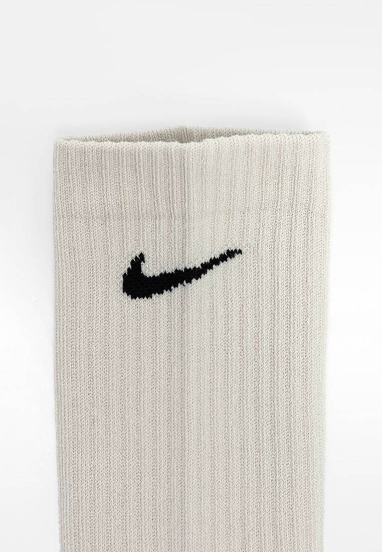 Chaussette en tricot côtelé beige avec un logo Nike Swoosh noir au niveau de la cheville. Le matériau semble doux et texturé.