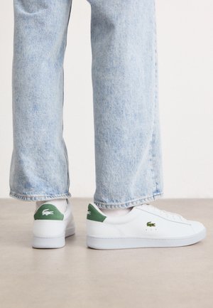 Hvide lædersneakers med grønne accenter på hælen og broderet logo. Glat tekstur, lavt design, parret med lyseblå jeans.