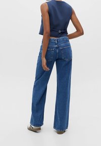 Jean en denim bleu à jambe large avec une taille haute, un léger délavage et des poches arrière. Assorti à un haut ajusté navy avec un détail au dos.