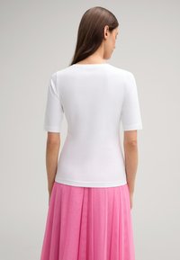 Weißes T-Shirt mit kurzen Ärmeln, Rundhalsausschnitt, taillierter Form und glatter Textur, getragen mit einem fließenden rosa Rock.