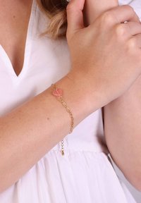 Gouden armband met een roze hartvormige edelsteen, uitgerust met een delicate schakeldesign en een verstelbare sluiting. Draagt om een lichte huidtonen pols.