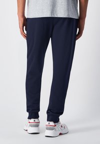Pantalones de chándal navy con puños elásticos y un ajuste relajado, hechos de material de algodón suave. Combinados con zapatillas deportivas blancas con acentos rojos.