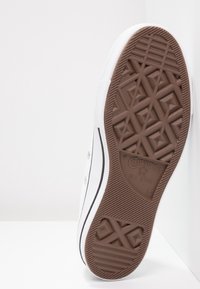 Baskets en toile blanches avec une semelle en caoutchouc brun, présentant un motif géométrique texturé, un contour noir le long des bords et des œillets en argent.