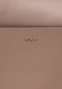 Materiale in pelle rosa caratterizzato da una superficie texturizzata e un sottile logo metallico dorato "abro" impresso su di esso.