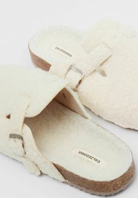 Witte pluizige instapsandalen met een band en metalen gesp, met een gevoerde zool en een gestructureerde kurken buitenzool. Etiket leest "CALZEDONIA."