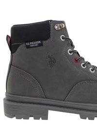 Tmavě šedé kotníkové boty U.S. Polo Assn. s černým polstrovaným límcem, kovovými očky, logem a robustní gumovou podrážkou.