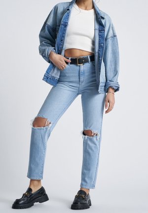 Vaaleansininen farkkutakki, valkoinen lyhyt toppi, vaaleansiniset kuluneet farkut, joissa on polviviat, sekä mustat loafersit, joissa on kultaiset yksityiskohdat.