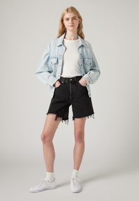 Light blue denim jacket over a white t-shirt, paired with high-waisted black shorts featuring frayed edges. White sneakers and socks complete the look.