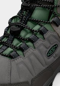 Γκρι πεζοπορικό παπούτσι με πράσινα υφασμάτινα πάνελ, διαθέτει μαύρα κορδόνια και ρυθμιζόμενα κλείσιμο με τόγκερ. Σχεδιασμένο με ανθεκτική σόλα και υφή για πρόσθετη σταθερότητα.