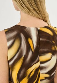 Mouwloze jurk met een draaiend patroon in bruin, geel en crème, met een knoopsluiting aan de achterkant en een gladde stofstructuur.
