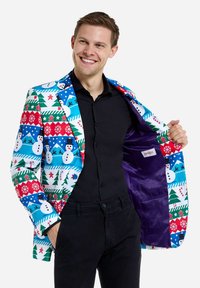 Färgglad högtidsblazer med mönster av snögubbar, träd och pepparkakor på en ljusblå, röd och grön bakgrund. Lila satinfoder.