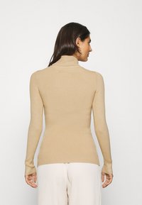 Beige ribbed turtleneck sweater with long sleeves and fitted silhouette. Soft texture, featuring a high neck and seamless design without embellishments.