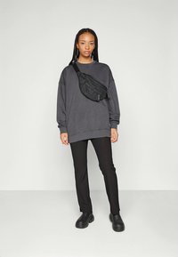 Grå oversized genser, sorte slim-fit bukser og sorte plattformsko. Magebelte båret diagonalt over torsoen. Minimalistisk design.