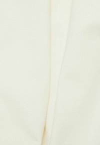 Tissu crème avec une texture douce, présentant des plis souples qui créent un drapé subtil, mettant en valeur son design léger et fluide.