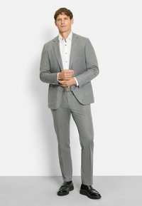 Grau maßgeschneiderter Anzug aus strukturiertem Stoff, schlanke Passform, weißes Hemd und schwarze Schuhe. Verfügt über subtile Streifen und metallische Akzente.