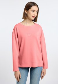 Lichtroze sweatshirt met een relaxte pasvorm, voorzien van een geborduurd hartlogo in het midden en een geribbelde halslijn. Lange mouwen met manchetten.