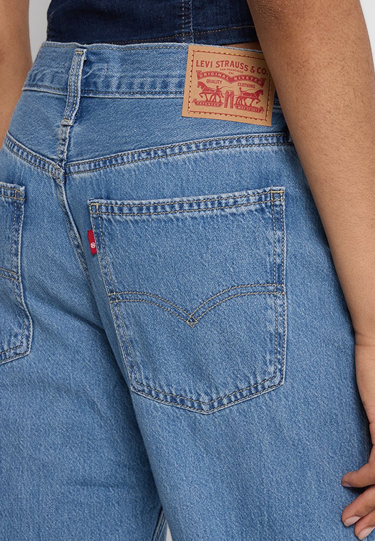 Person in blauen Levi's Jeans, die Details der hinteren Tasche zeigen, Leder-Brand-Patch und rotes Levi's-Tag an der Tasche.