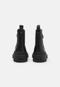 Schwarze Lederstiefeletten mit runder Spitze, massiver Sohle, Ziehschlaufen und geprägtem "COACH"-Logo an der Ferse. Matte Oberfläche, modernes Design.