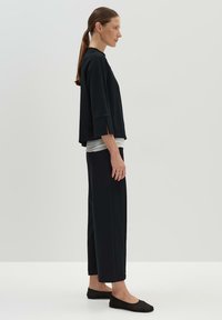 Haut noir ample avec un col montant et des manches trois-quarts, associé à un pantalon noir à jambes larges et des chaussures plates noires. Texture lisse.