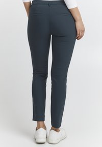 Tmavě modré slim-fit kalhoty vyrobené z měkké tkaniny, s dvěma zadními kapsami a čistým lemem, nošené s bílými teniskami.
