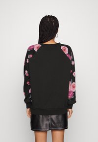 Černá mikina s květinovým vzorem na rukávech, s kulatým výstřihem a žebrovanými manžetami. Hladká textura, volný střih.