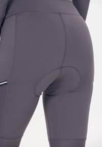 Nærbillede af grå polstrede cykelshorts, der bæres, med forstærkede syninger og meshpanel på låret.