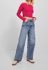 Åtsittande, kortärmad rosa topp som är matchad med högmidjade, vida ljusblå jeans och beigea slip-on skor. Enkel, avslappnad estetik.