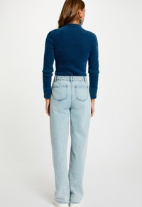 Maglione blu a trama con maniche lunghe abbinato a jeans chiari a vita alta. Presenta un design semplice e colori a contrasto.