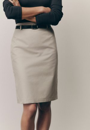 Beige penkjol i ett texturerat tyg, med en strömlinjeformad design och ett svart bälte, vilket ger en skräddarsydd look runt midjan.