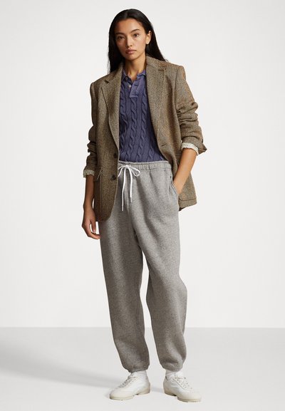 Blazer en chevrons marron sur un pull marin en tricot torsadé, associé à un pantalon de survêtement gris et des baskets blanches. Tenue décontractée superposée avec des textures distinctes.