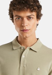 Polo de color verde claro hecho de tejido texturizado, con una tapeta de tres botones y un pequeño logo blanco en el pecho.