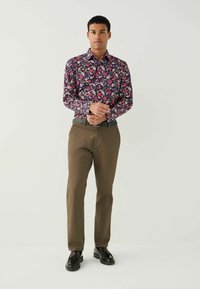 Bloemshirt in donkerpaars met roze en witte bloemen; gecombineerd met lichtbruine broeken en zwarte schoenen; gladde stof en klassieke pasvorm.