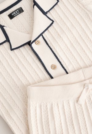 Ensemble de vêtements d'intérieur en maille couleur crème avec un design côtelé, un galon contrastant bleu marine, deux boutons en bois sur le polo et une taille élastiquée.