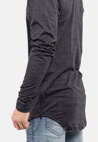 Langärmliges, schiefergraues Hemd aus weichem Stoff, mit abgerundetem Saum und Reißverschlussdetails an der Seite, kombiniert mit hellblauen Jeans.