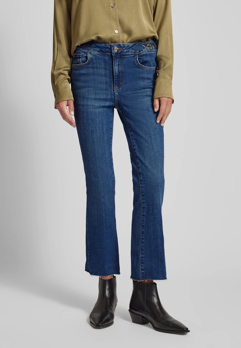 Jeans blu scuro con design a gamba dritta, caratterizzati da un orlo sfrangiato, cinque tasche e accessori metallici. Abbinati a stivaletti neri alla caviglia.